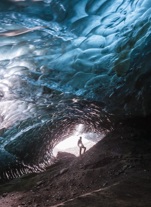 A glacier guide standing at the entrance of an blue ice cave in Iceland