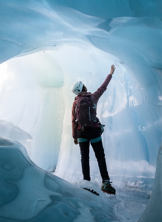 A glacier guide reaching up to the ceiling of a blue ice cave