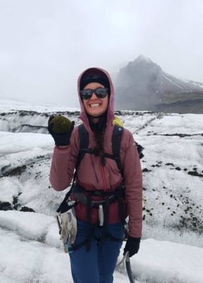 A girl on the glacier, poses with a massive glacier mouse (rock that is fully covered with moss)