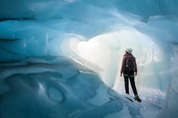 A certified glacier guide stands at the entrance of a blue ice cave on an exclusive ice cave tour
