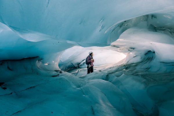 A certified glacier guide standing in the incredibly blue ice cave