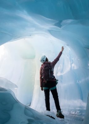 A certified glacier guide reaches up and touches the wall of a blue ice cave
