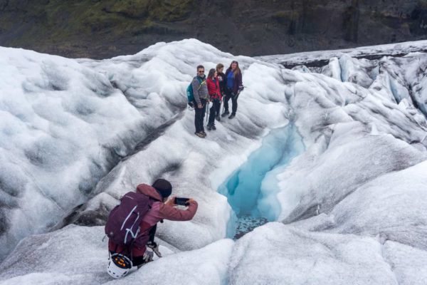 A certified glacier guide, takes a photo for her group next to a beautiful, crystal blue pool on the glacier.