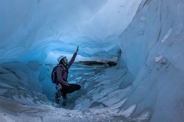 A certified glacier guide, crouches down in the more narrow part on her blue ice cave tour