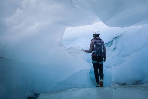 A certified guide walks through the blue ice cave, touching the ice wall on her left side.
