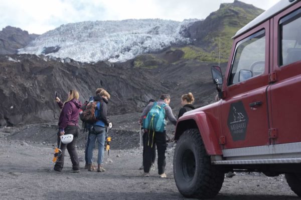 A group stands next to a red Land Rover Defender at the bottom of the glacier