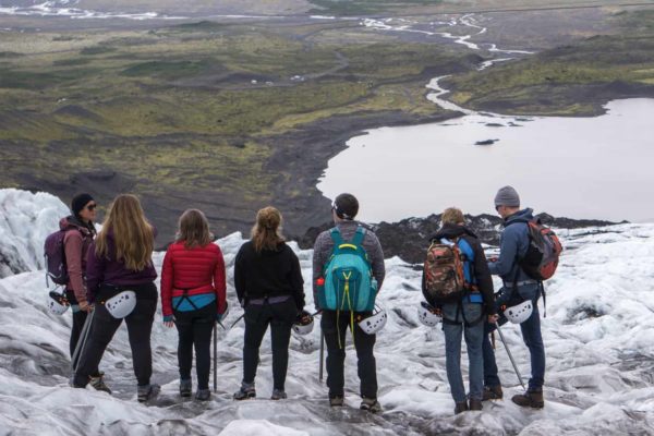 A group on a glacier adventure stands on the glacier, overlooking the glacier lagoon and vast sand fields
