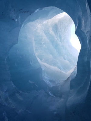 light shining through an opening of a small blue ice cave