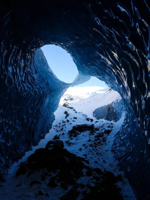 light shining through the entrance of a large, black and blue ice cave - melrakki adventures