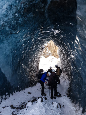 a group of people spread around in a tall blue ice cave