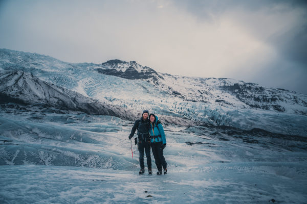 two people standing on a blue ice on top of a glacier. icefall covered with snow can be seen in the background
