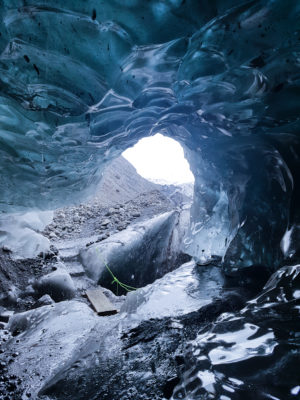 a small bridge extending over a crevasse in front of an ice cave. photo taken from inside the blue ice cave.
